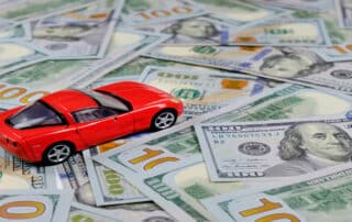 Red toy car on cash representing auto loans, RV financing, car title registration, and vehicle ownership costs.