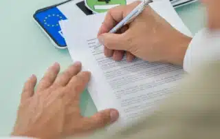 Person signing a legal document with a pen at a desk, representing Montana LLC vehicle registration compliance. Image reflects paperwork, ownership documentation, and legal requirements involved in properly registering a vehicle under a limited liability company.