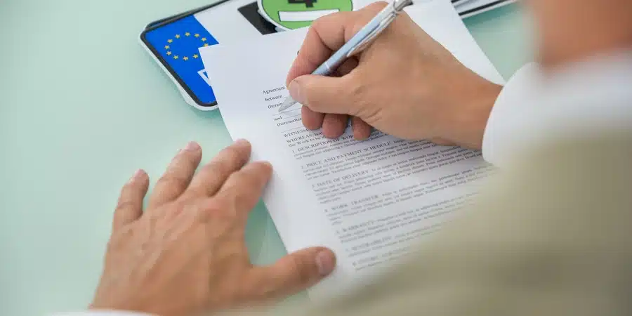 Person signing a legal document with a pen at a desk, representing Montana LLC vehicle registration compliance. Image reflects paperwork, ownership documentation, and legal requirements involved in properly registering a vehicle under a limited liability company.