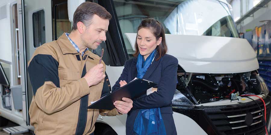 Two mechanics reviewing repair details beside an RV, representing questions about out-of-state inspection rules and when, if ever, Montana requires inspections for RVs registered or maintained under Montana regulations.